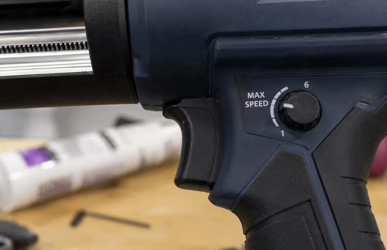 Close-up of a cordless caulking gun speed control trigger and adjustable maximum speed dial used to regulate sealant dispensing flow